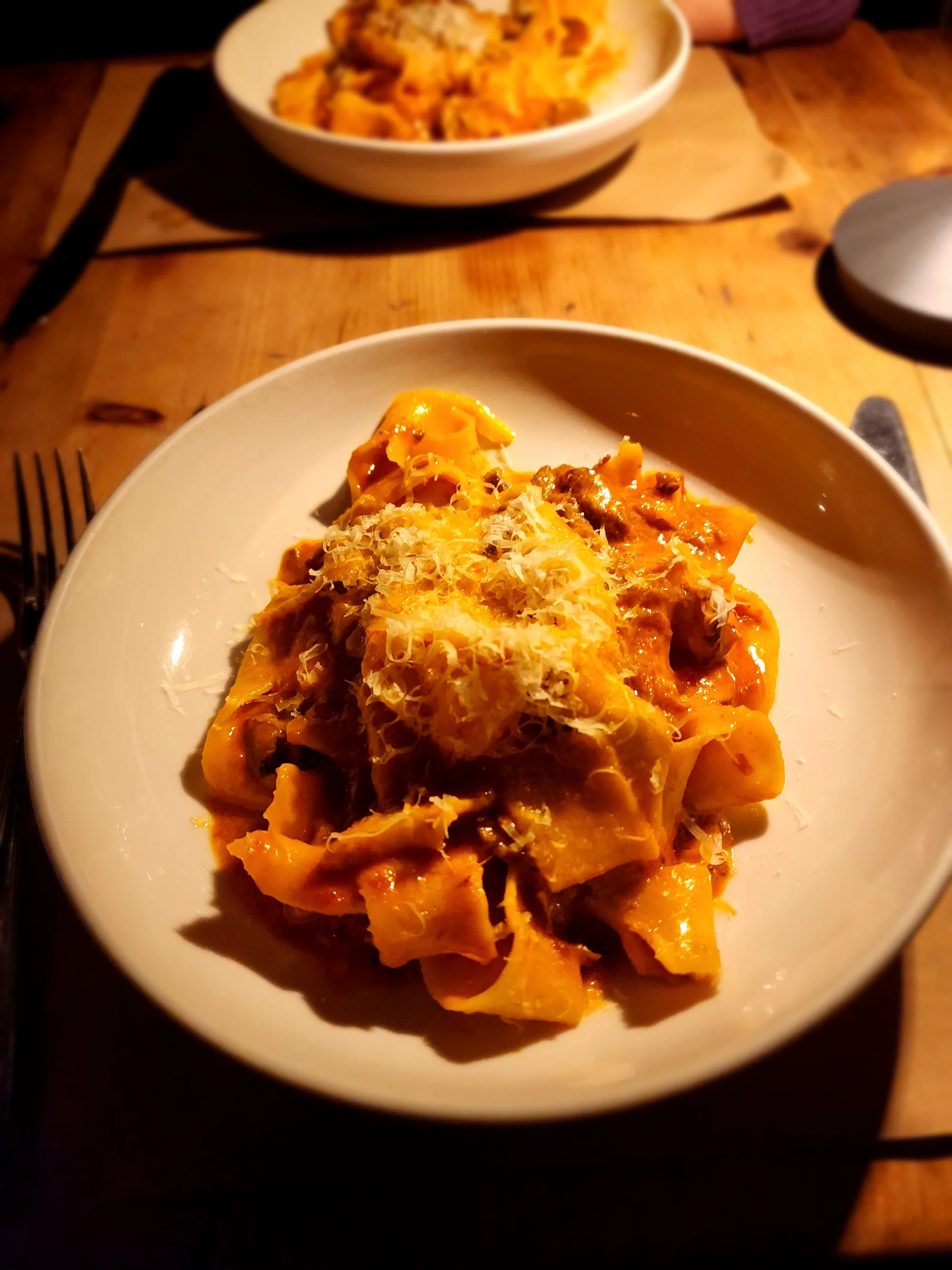 Ribbon pasta with ragu and grated cheese in a white bowl on a warmly lit wooden table