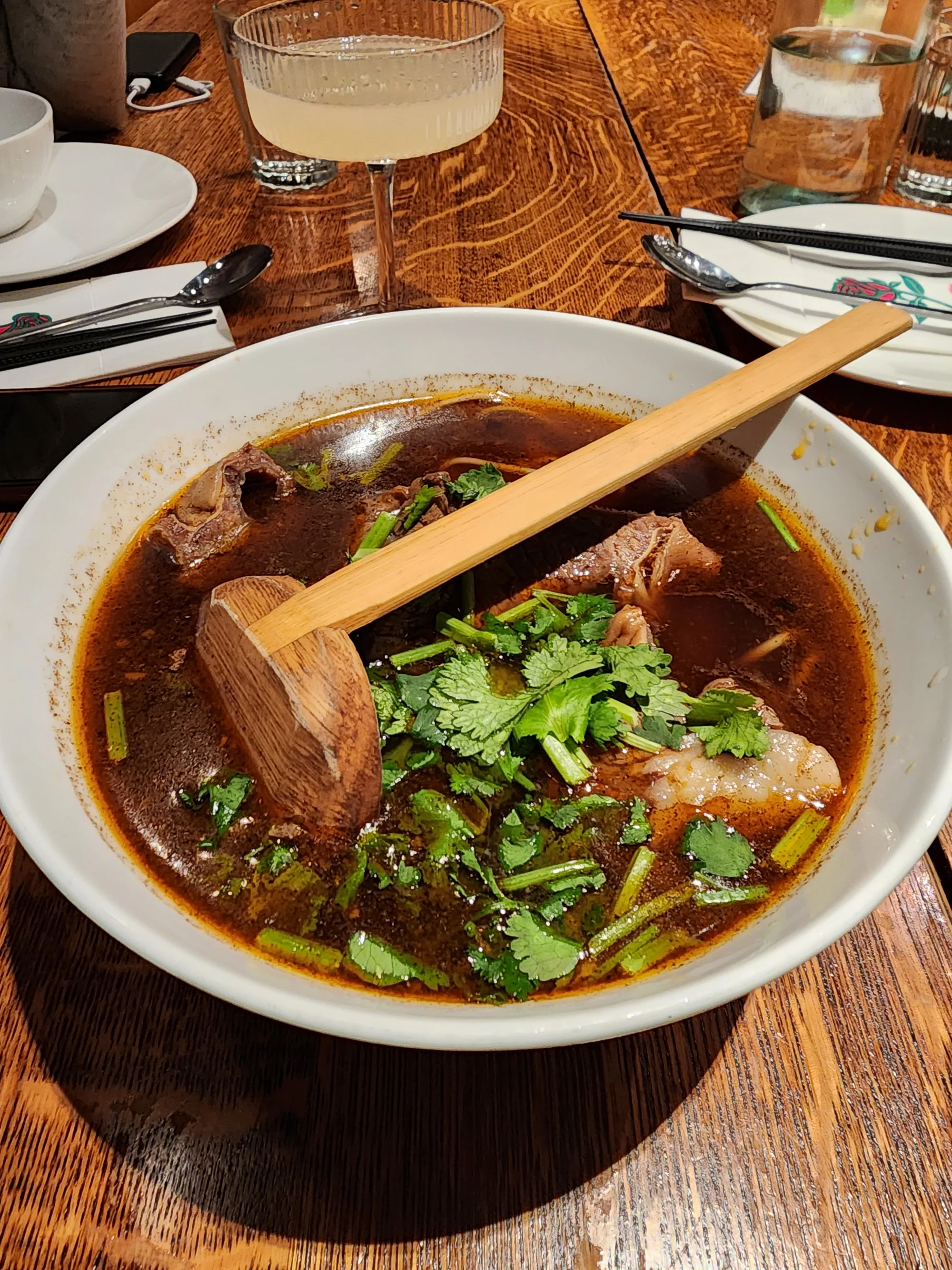 Beef noodle soup with cilantro and a wooden ladle resting across the bowl