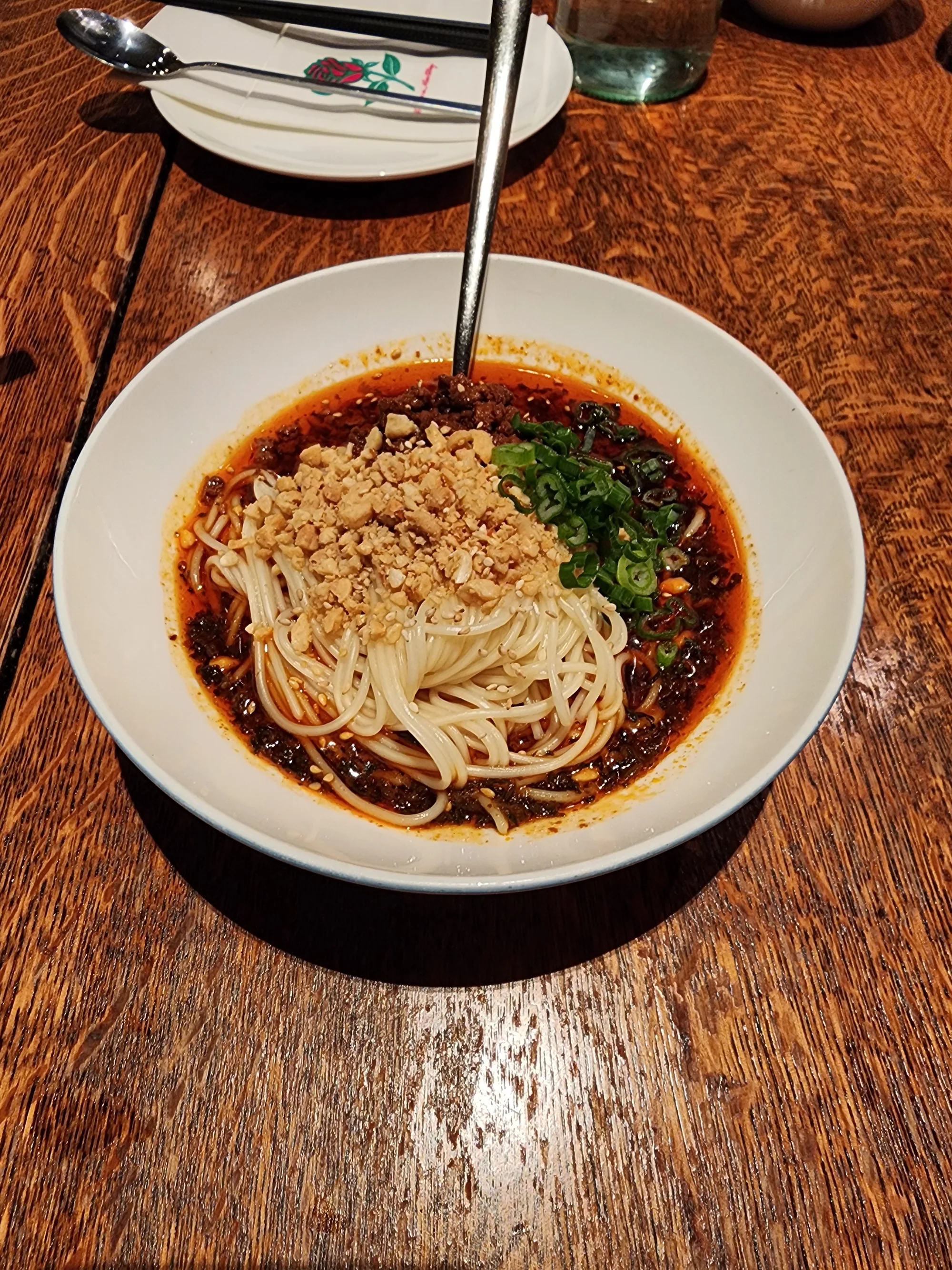 Noodles with a crumbled topping and scallions in a white bowl