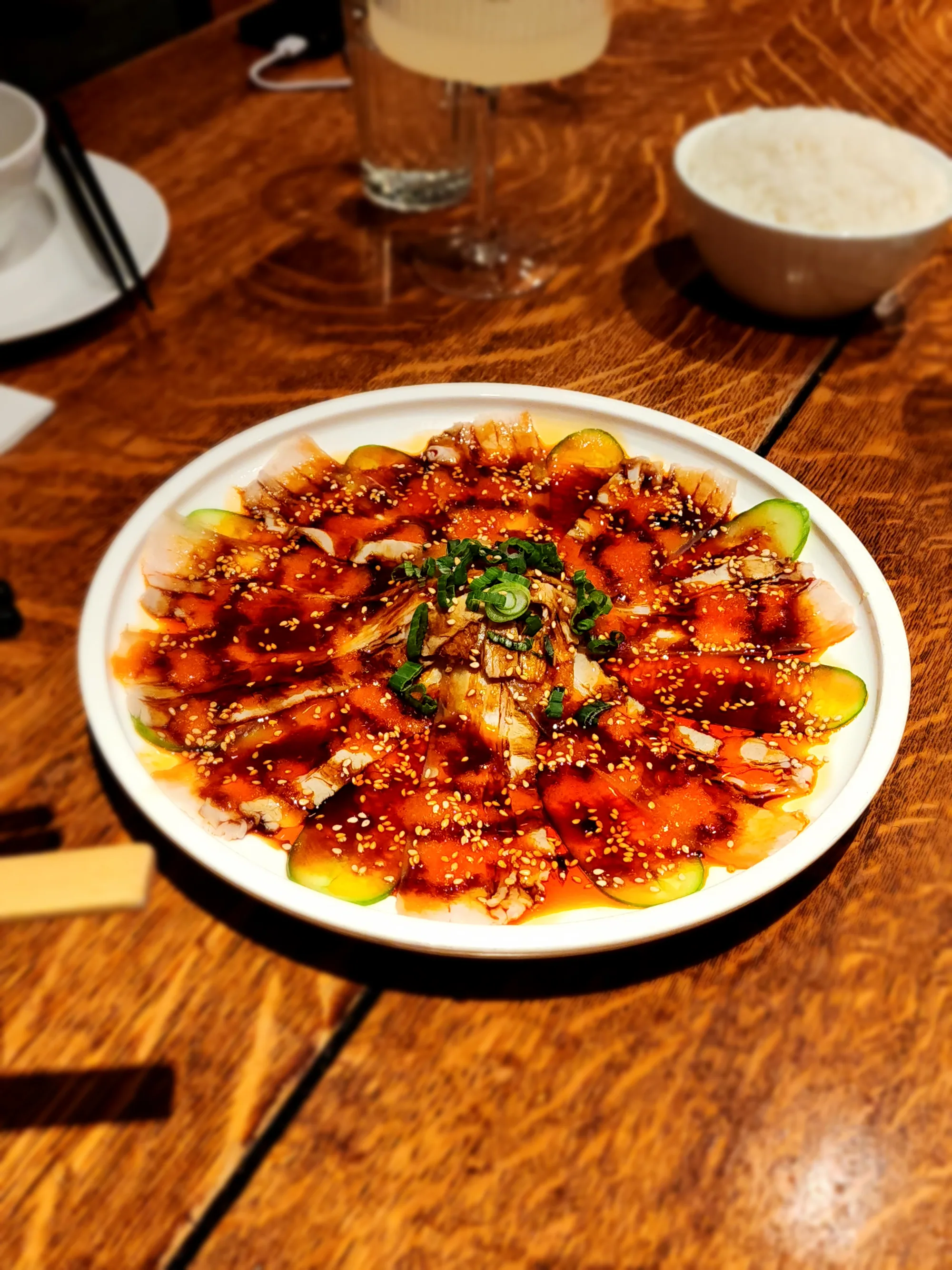 Pork belly slices and cucumber arranged in a ring with chili sauce, sesame, and scallions